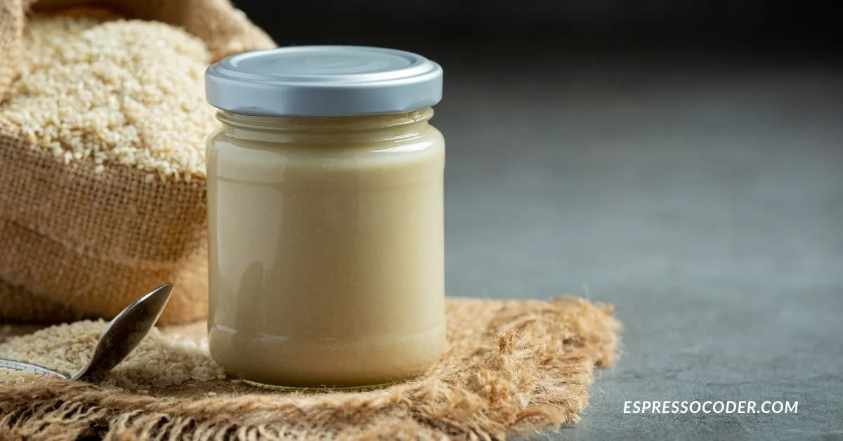 Jar of tahhiini sesame paste with spoon on rustic table.